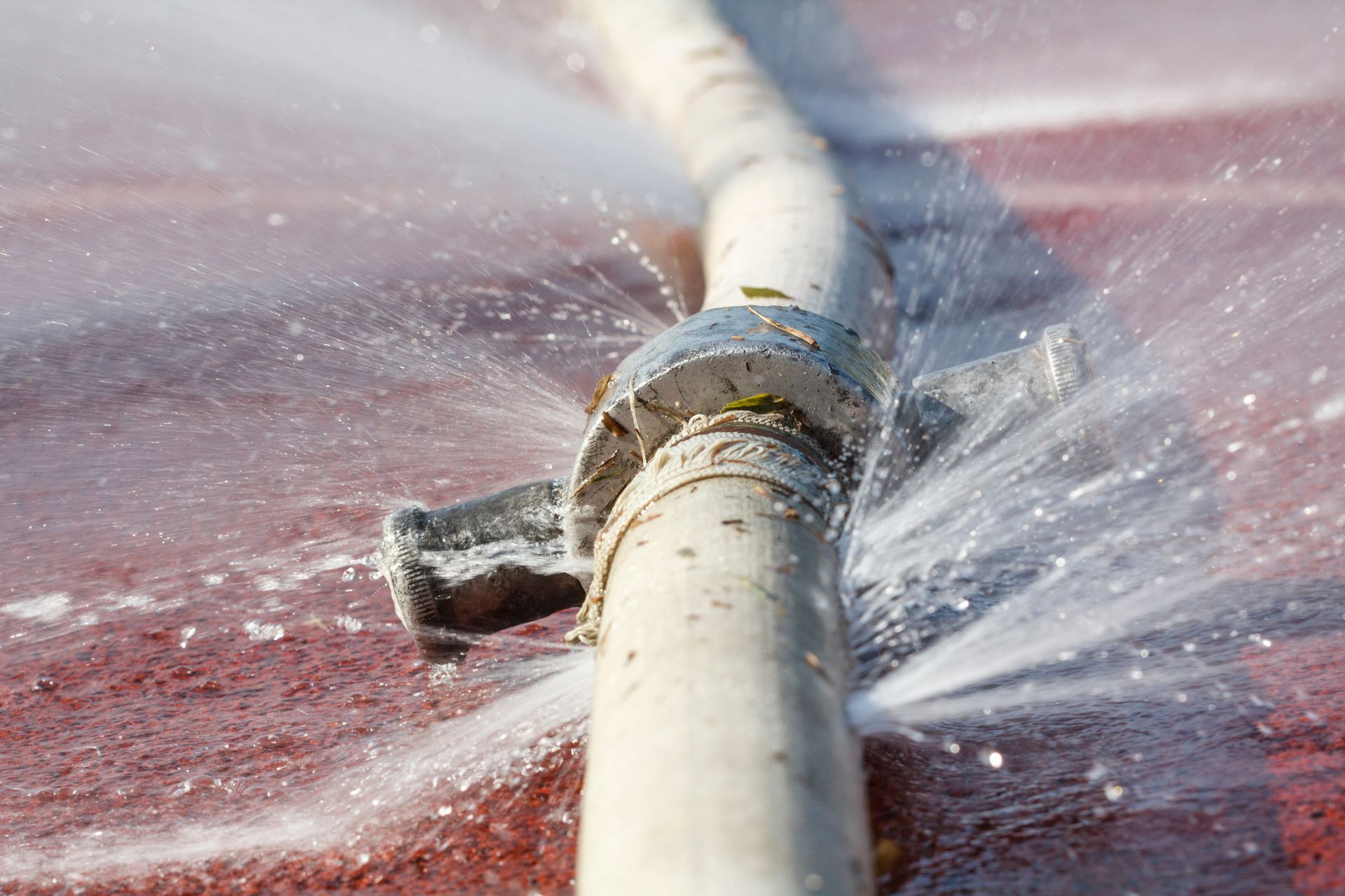 Burst pipe spraying water across a red surface under a white hose