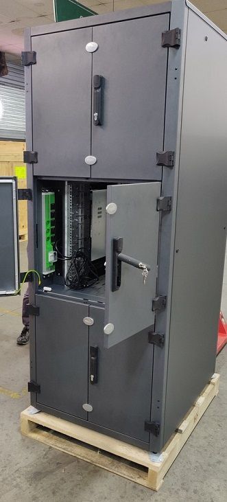 Une grande armoire industrielle grise, munie de plusieurs portes verrouillables, repose sur une palette en bois, la porte centrale restant ouverte.