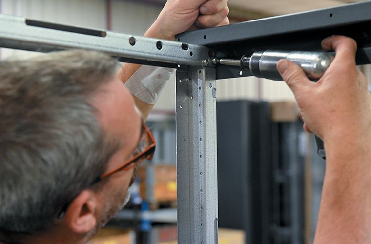Une personne utilise une perceuse électrique pour assembler des composants de charpente métallique dans un entrepôt.