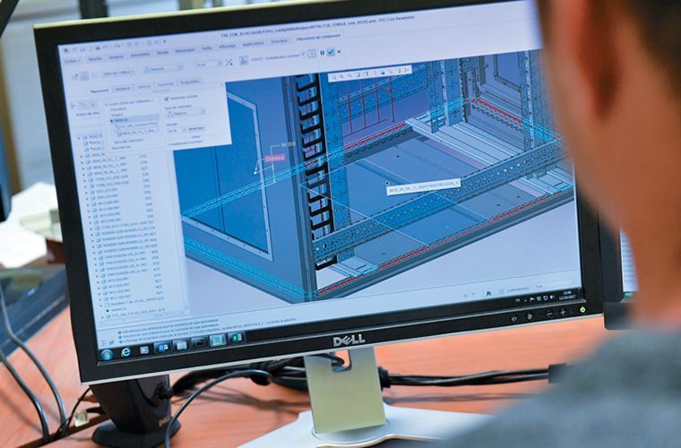 Une personne visualise un dessin CAO 3D sur un écran d'ordinateur, assise à son bureau.