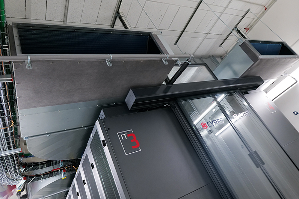 De grands conduits de ventilation industrielle CVC sont suspendus au-dessus d'une unité de machinerie gris foncé portant une étiquette numérotée rouge.