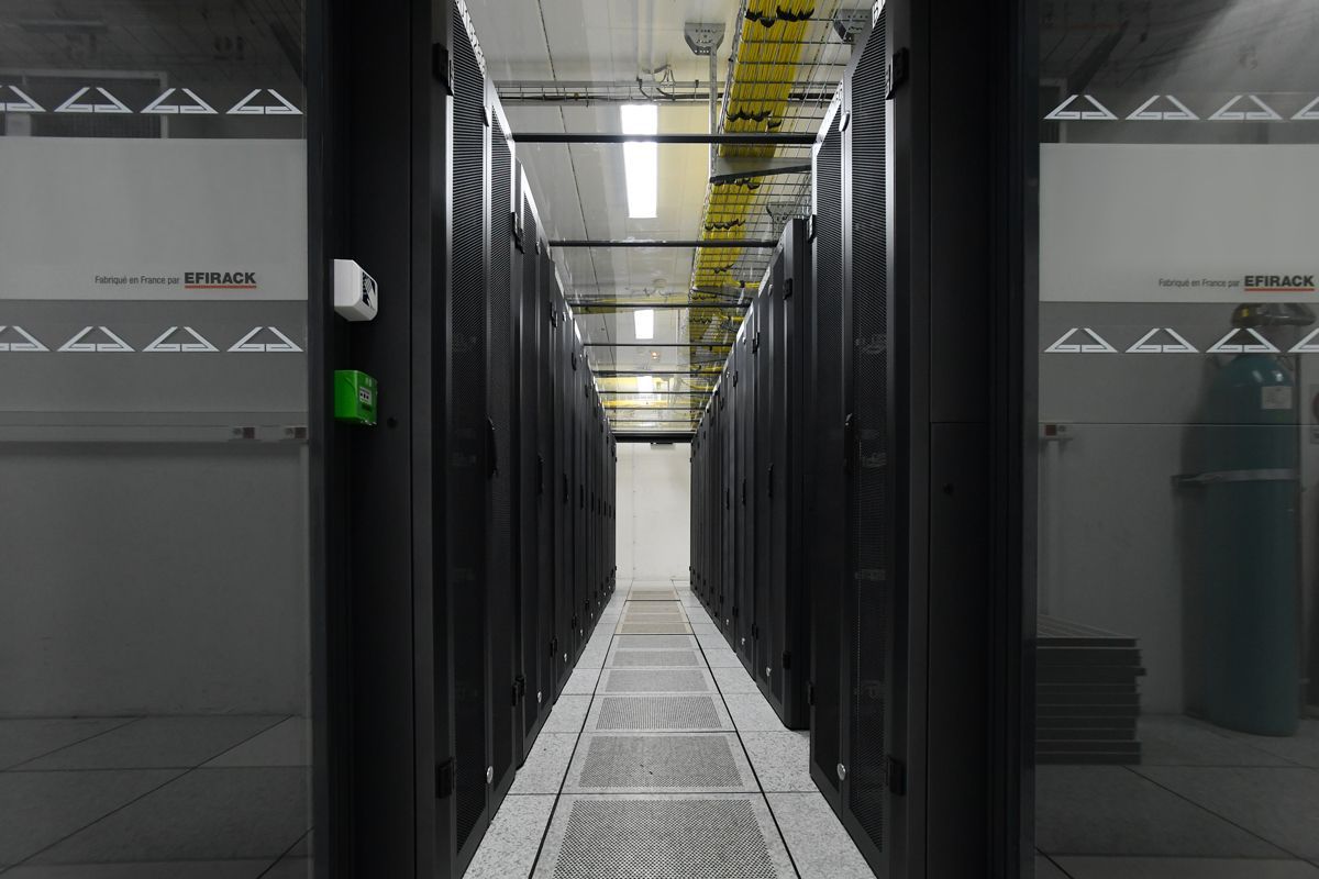 Une allée longue et étroite dans un centre de données, bordée de part et d'autre de rangées de hautes baies de serveurs noires.