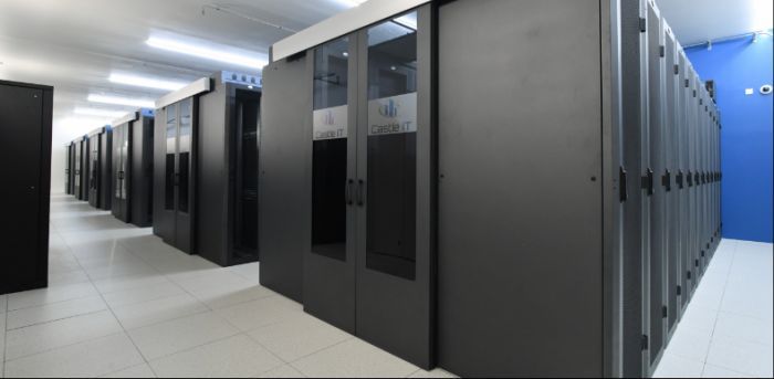 Des rangées de baies de serveurs noires dans un centre de données propre et lumineux, avec un sol clair et des murs bleus.