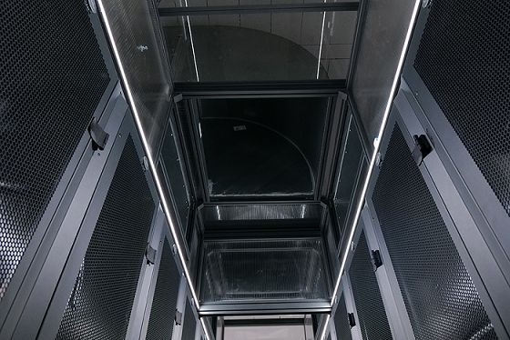 Vue en contre-plongée d'une allée sombre et métallique d'une salle serveur, avec de hauts panneaux perforés et un éclairage zénithal.