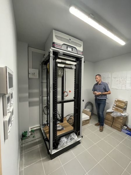 Une personne se tient debout dans une petite pièce carrelée, à côté d'une baie de serveurs vide sur laquelle est montée une unité de refroidissement.