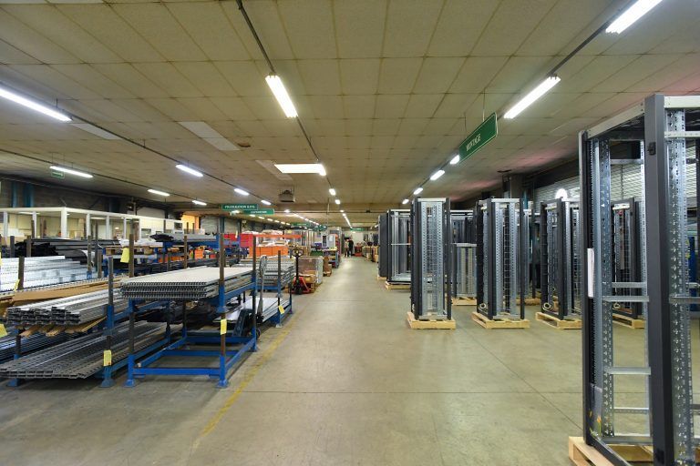 Intérieur spacieux d'un entrepôt industriel avec des rayonnages métalliques à gauche et des armoires serveurs verticales à droite.