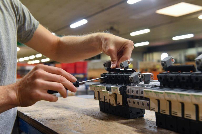 Une personne utilise un tournevis pour assembler des borniers électriques sur un établi dans un environnement industriel.
