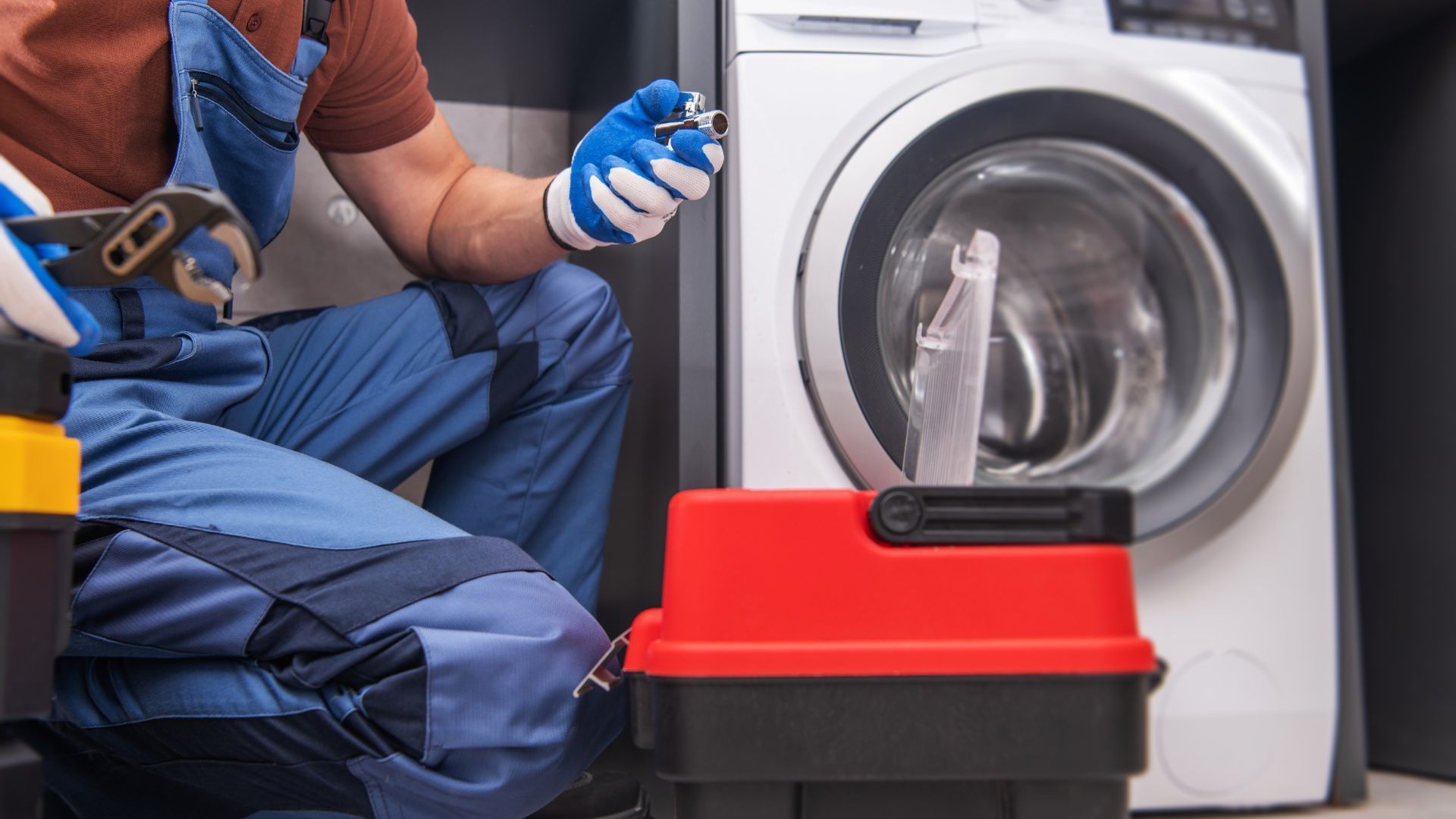 A man is kneeling down in front of a washing machine and fixing it.
