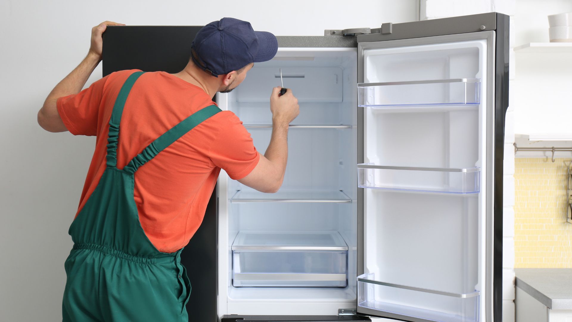 A man is fixing a refrigerator in a kitchen.