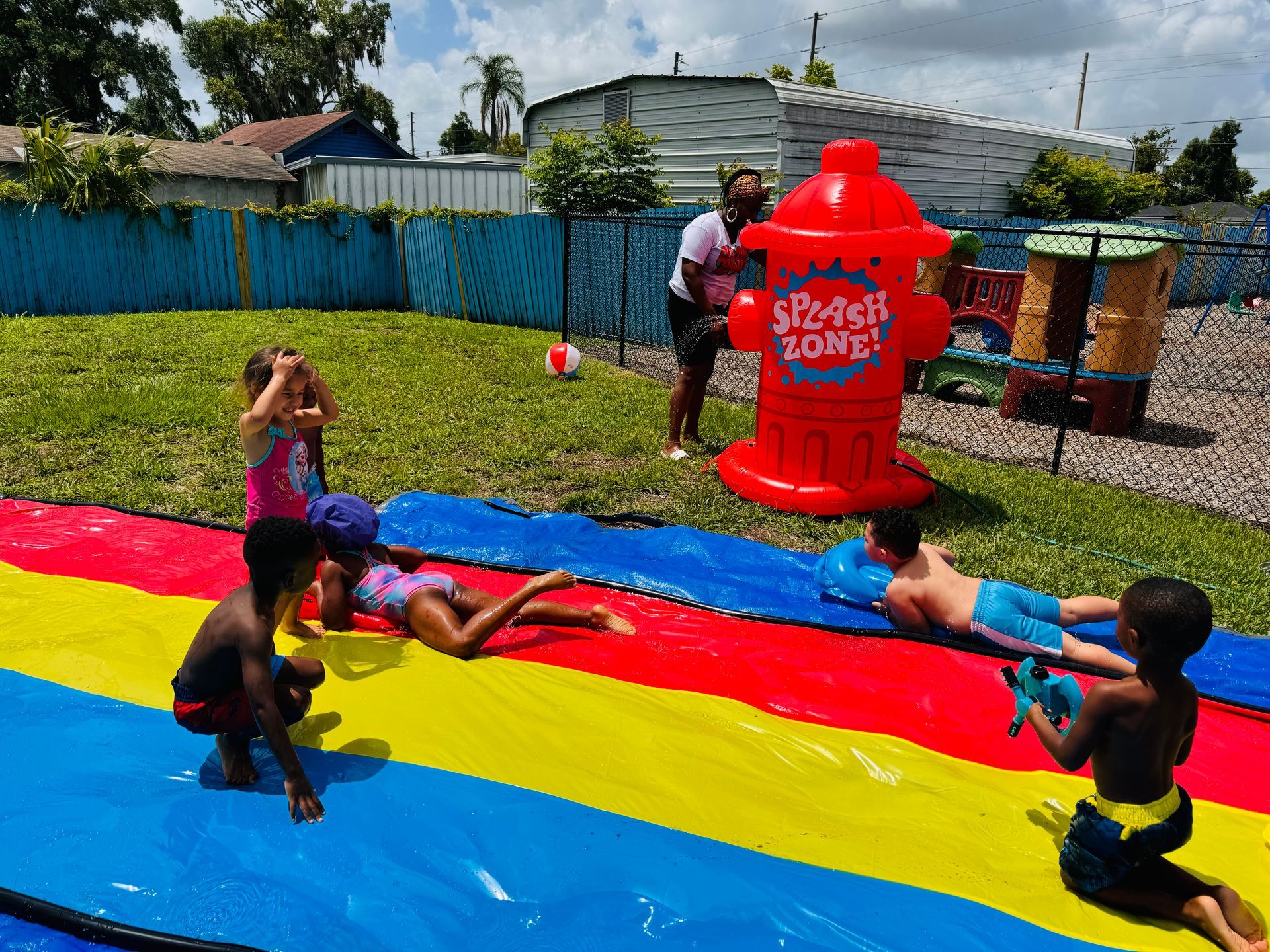 A group of children are playing on a water slide in a backyard.