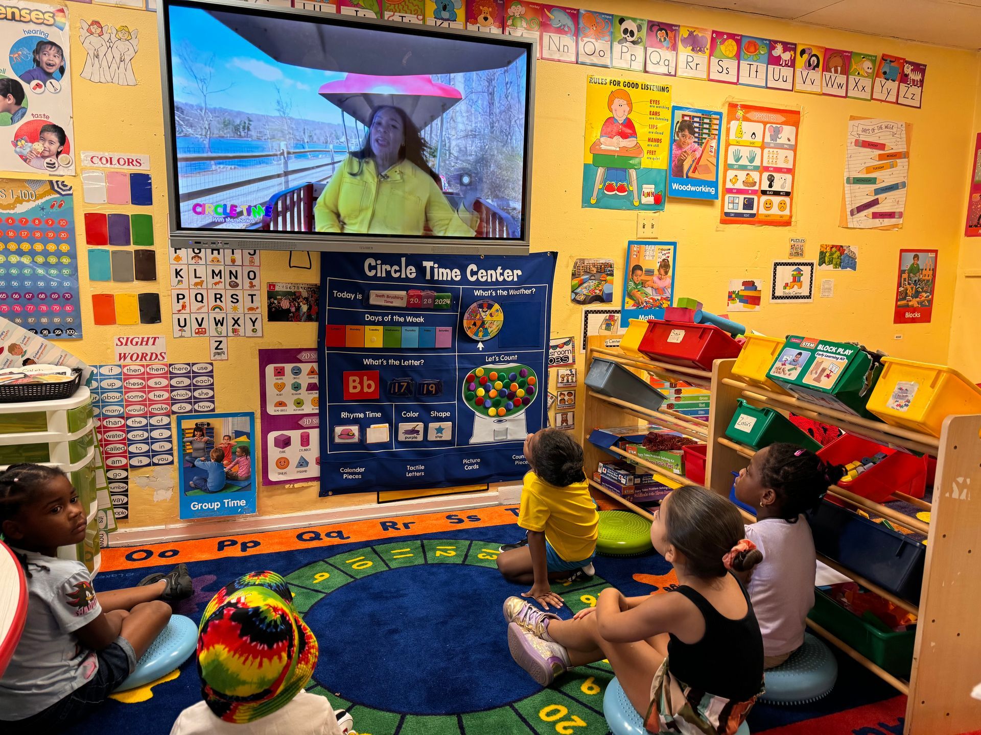 A group of children are sitting on the floor in a classroom watching a video.