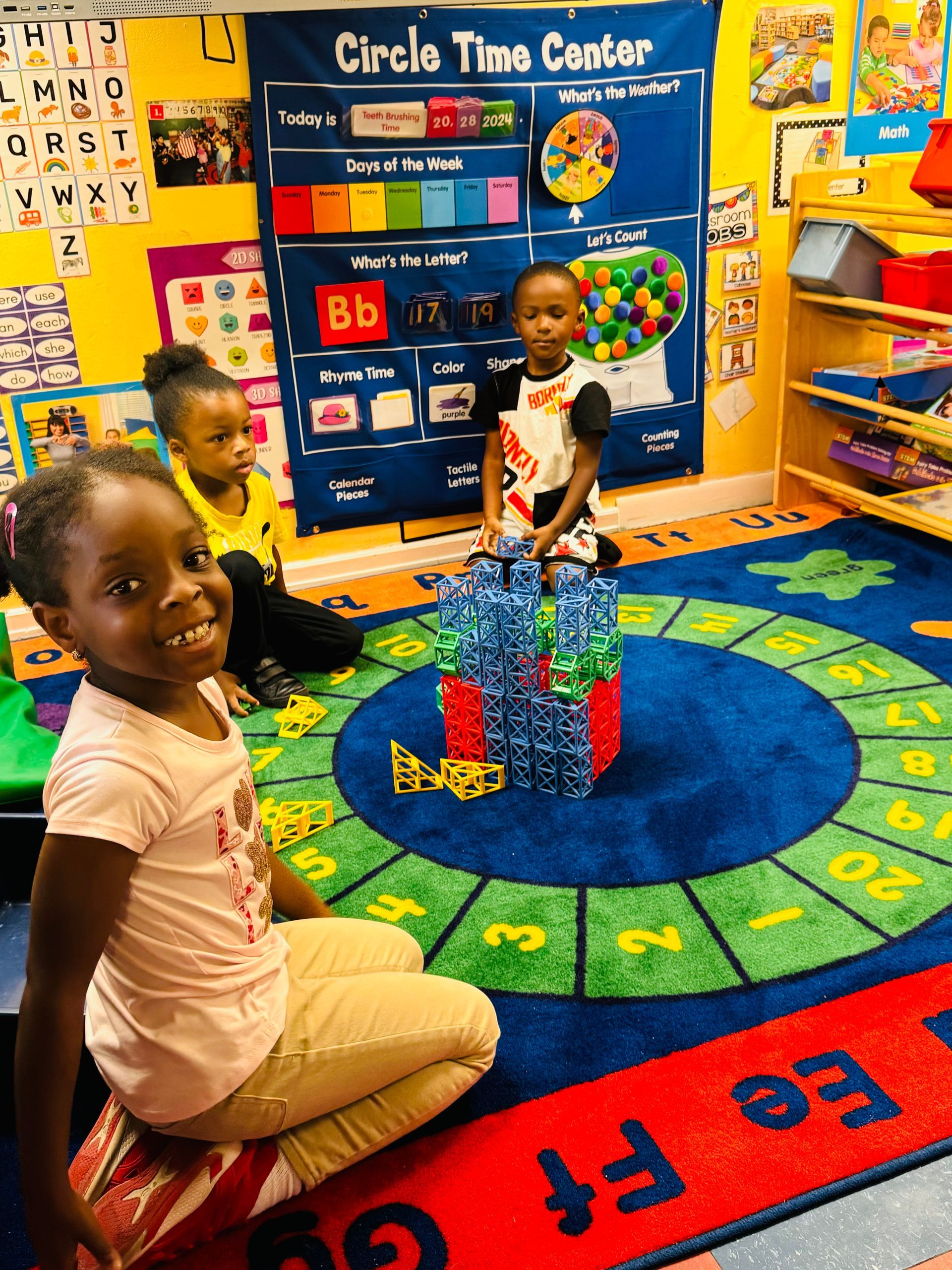 A group of children are sitting on the floor in a circle time center.