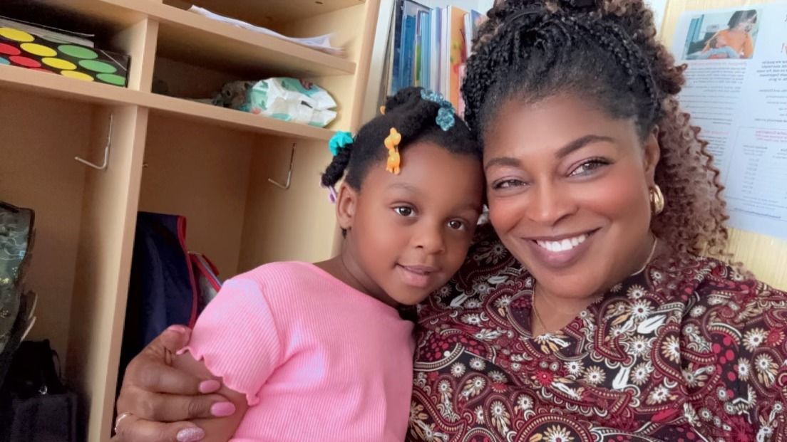 A woman is holding a little girl in her arms and they are smiling for the camera.