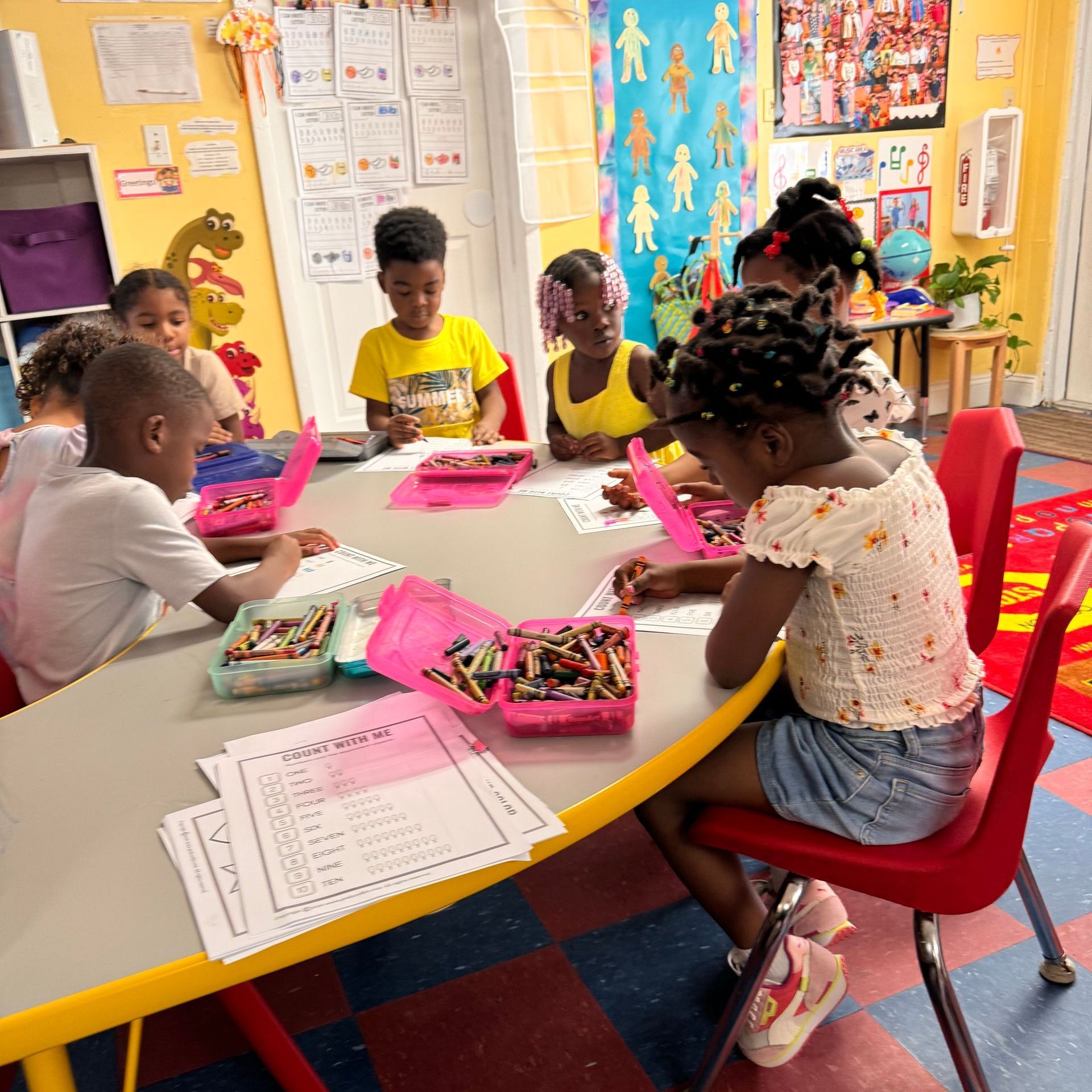A group of children are sitting around a table with crayons.
