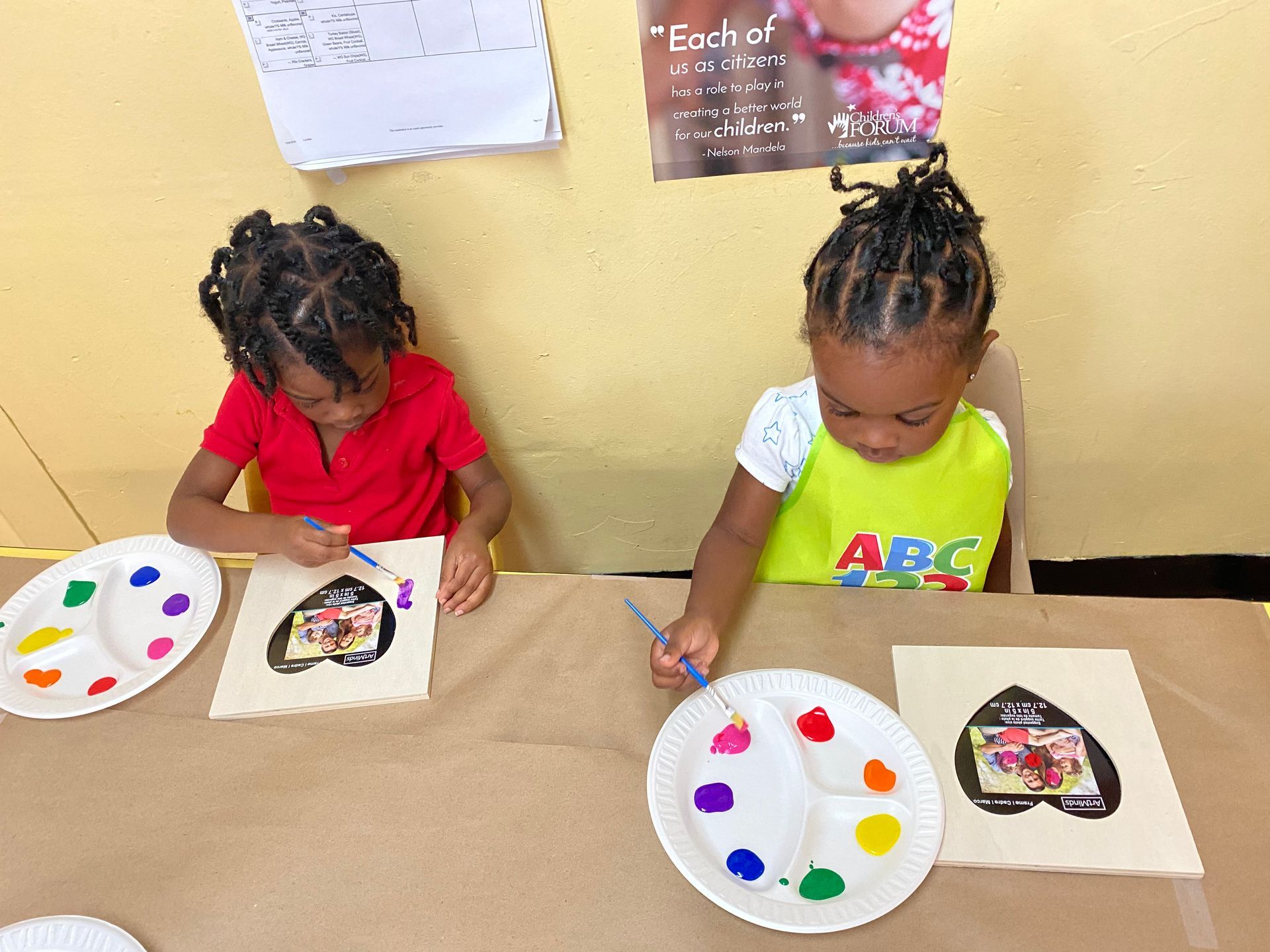 Two children are sitting at a table painting with paper plates.