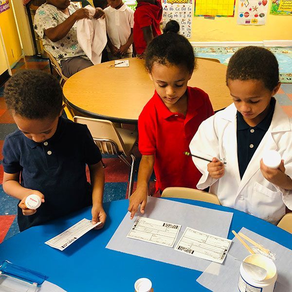 A group of children are sitting at a table looking at pills