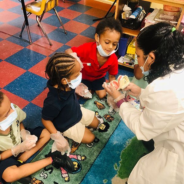 A group of children are sitting on the floor while a woman shows them a model of a tooth