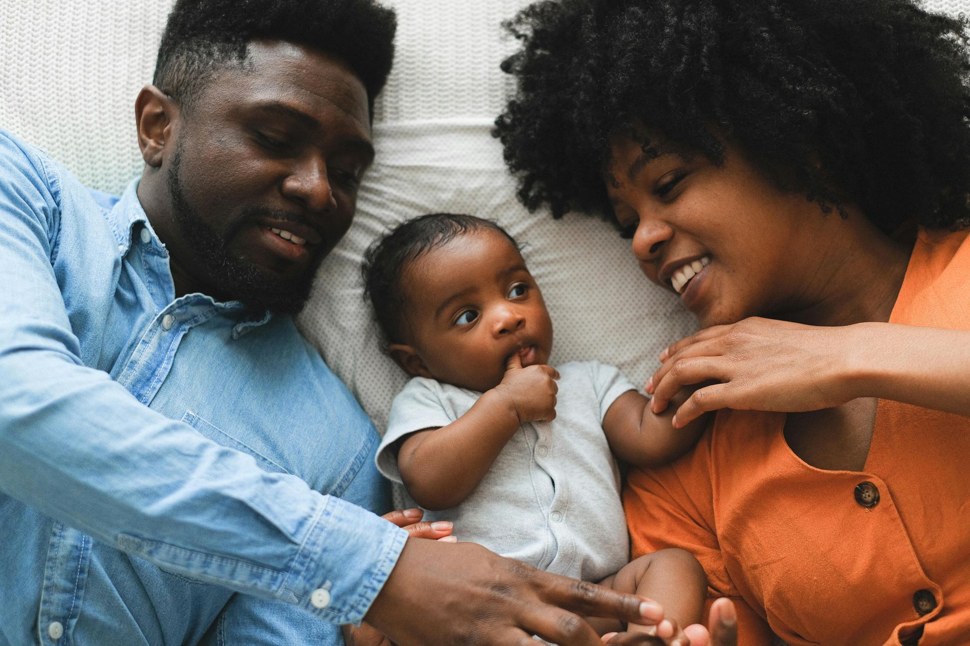 A man and woman are laying on a bed with a baby.