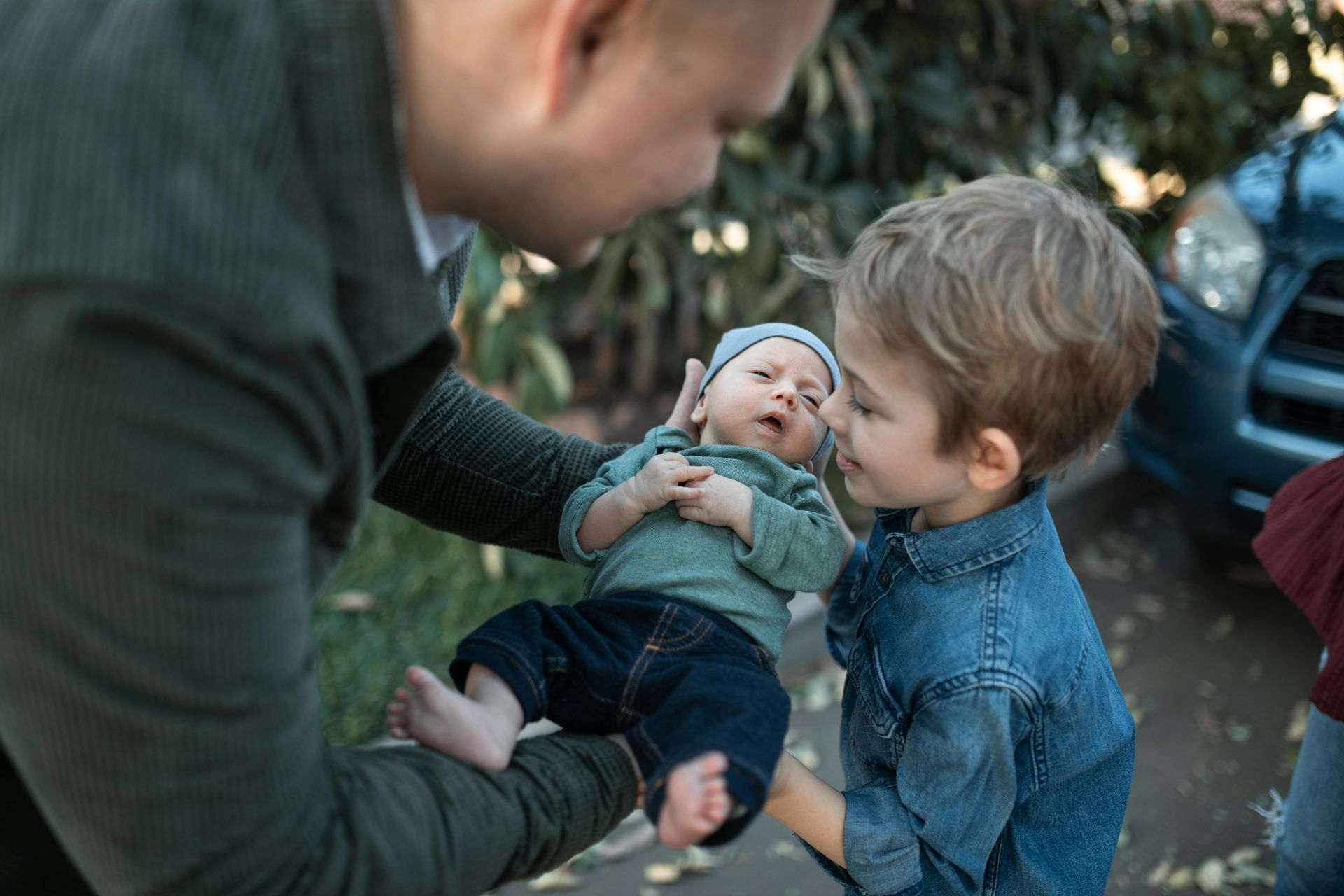 A man is holding a baby and two boys are looking at it.