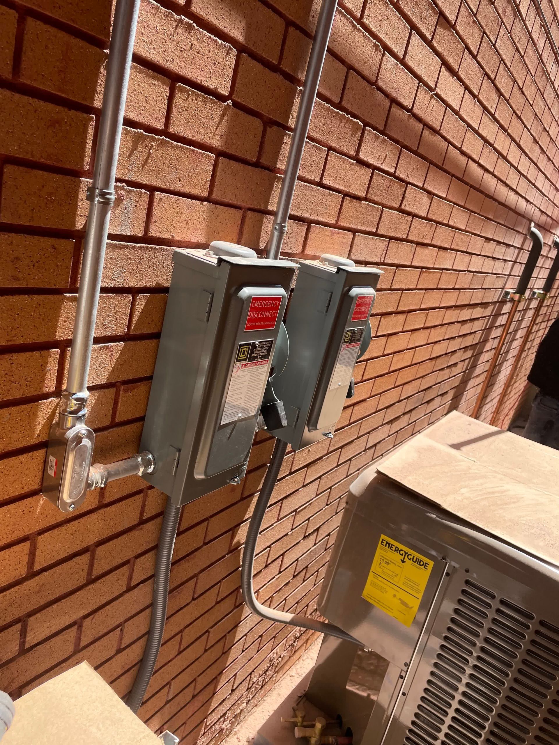 A brick wall with electrical boxes attached to it and an air conditioner.