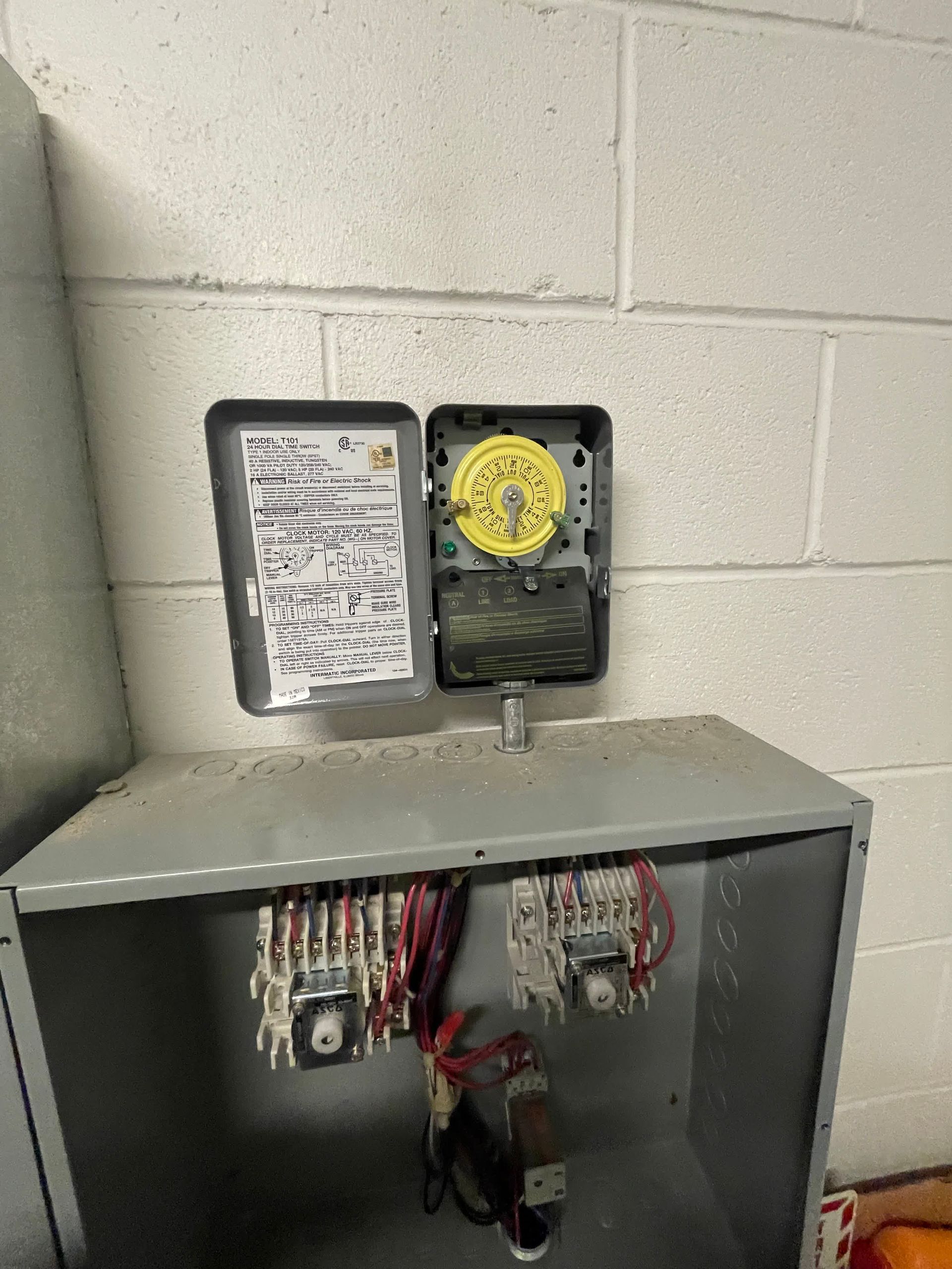 A clock is sitting on top of a metal box next to a brick wall.