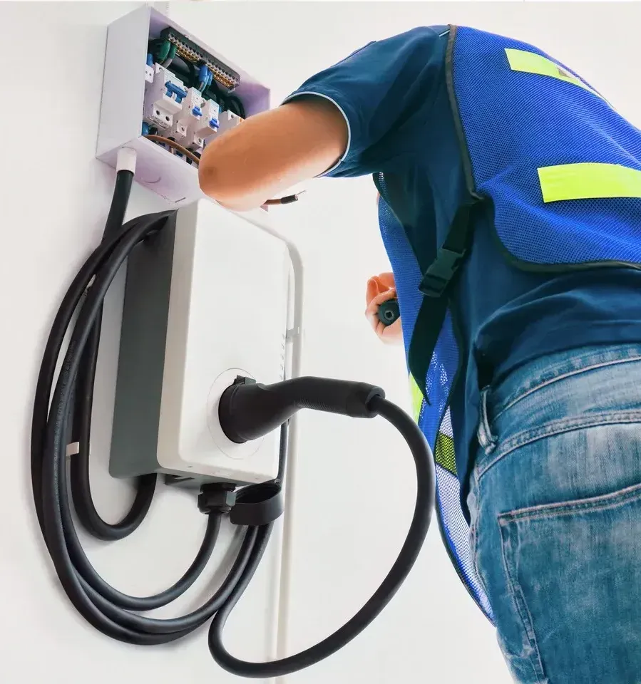 A man in a blue vest is working on an electric vehicle charging station