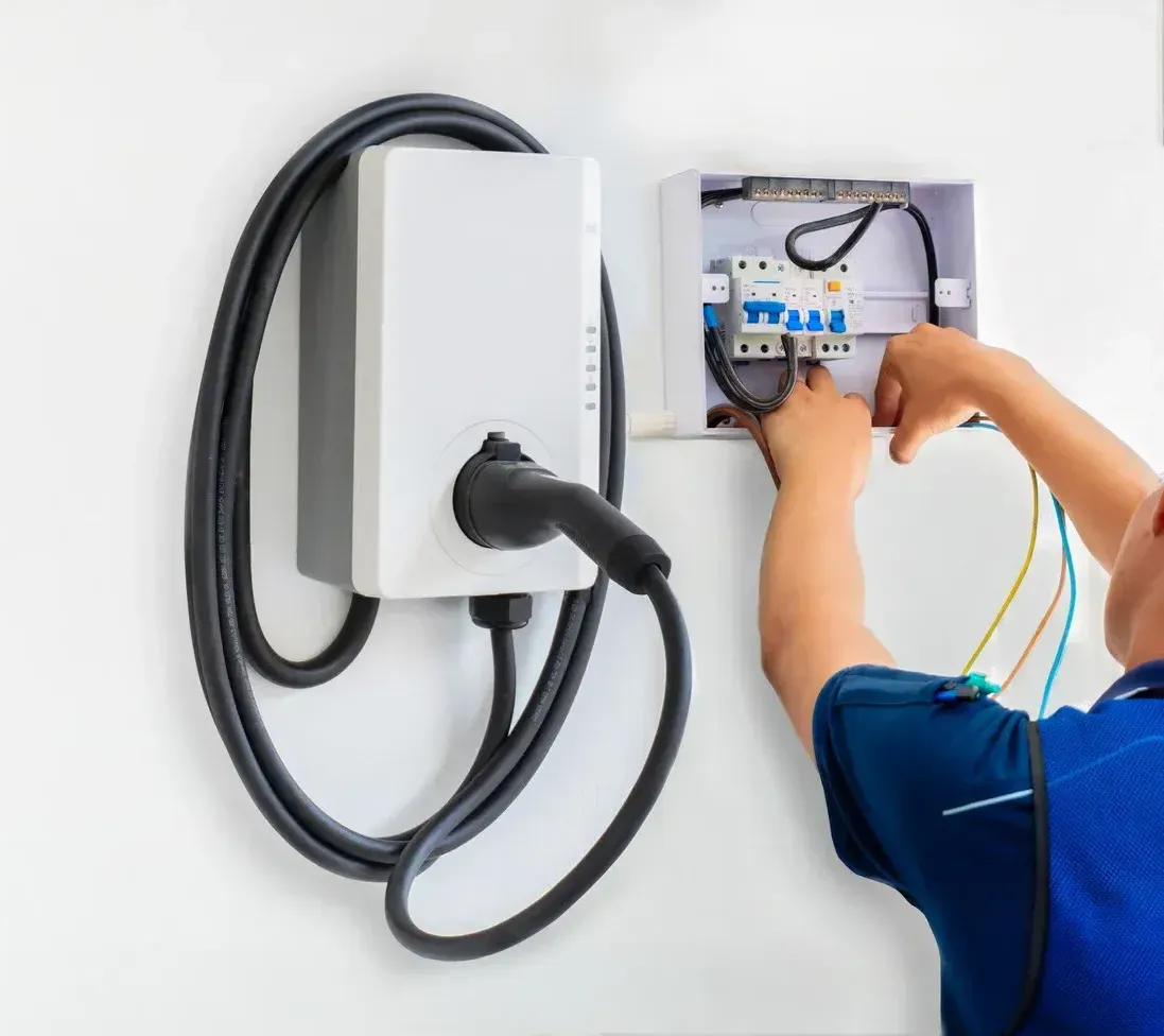 A man is working on an electric car charger on a wall.