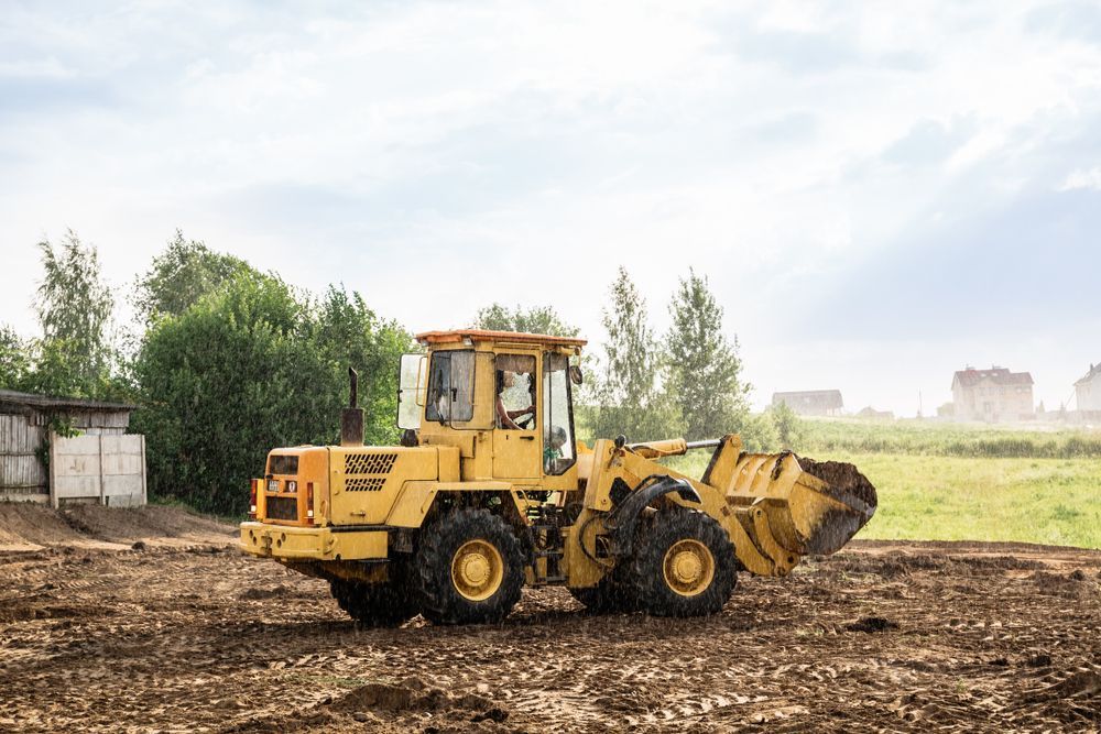 Yellow front loader on a muddy construction site under a bright sky