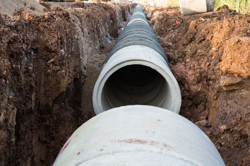 Large gray drainage pipes laid in a dirt trench at a construction site