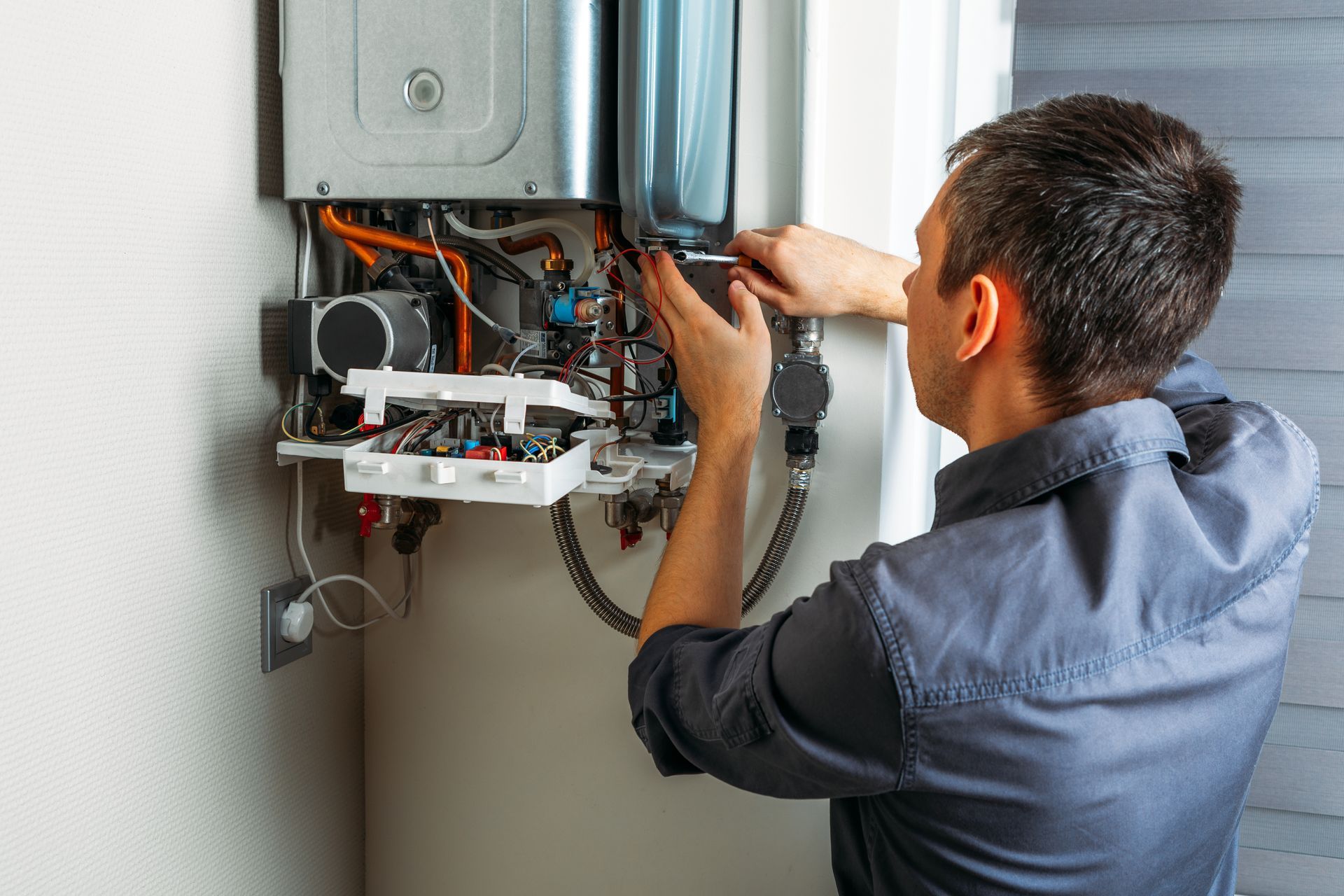 Technician repairing wall-mounted boiler with open front panel and exposed wiring