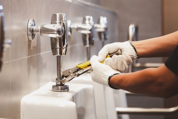 Plumber using a wrench to repair a leaking pipe under a sink sink cabinet