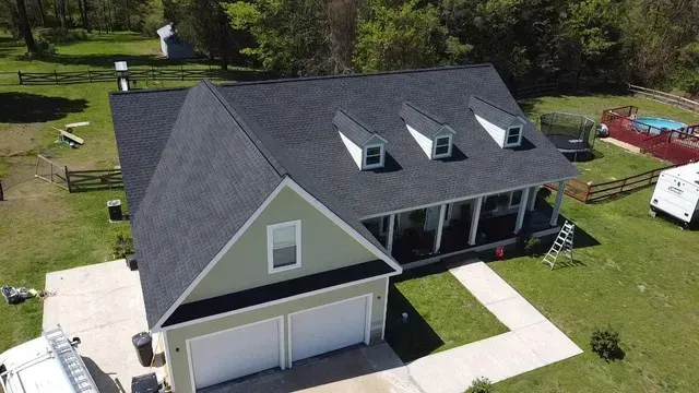 Aerial view of a house with a dark roof, green siding, and white garage doors on a sunny day.