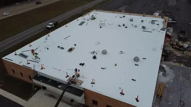 An aerial view of a large building with a white roof being installed.