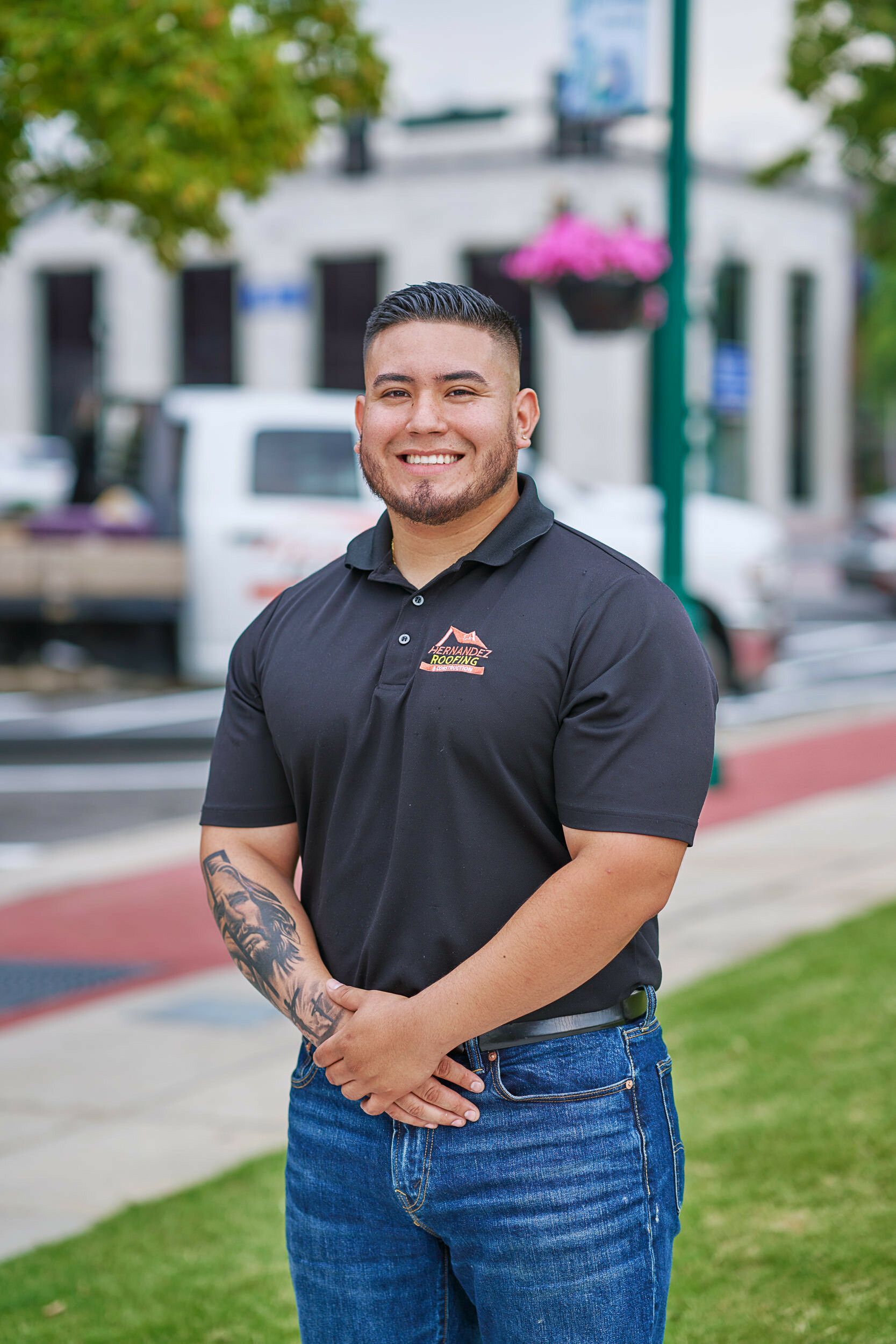 A man with a tattoo on his arm is standing in a park with his hands on his hips.