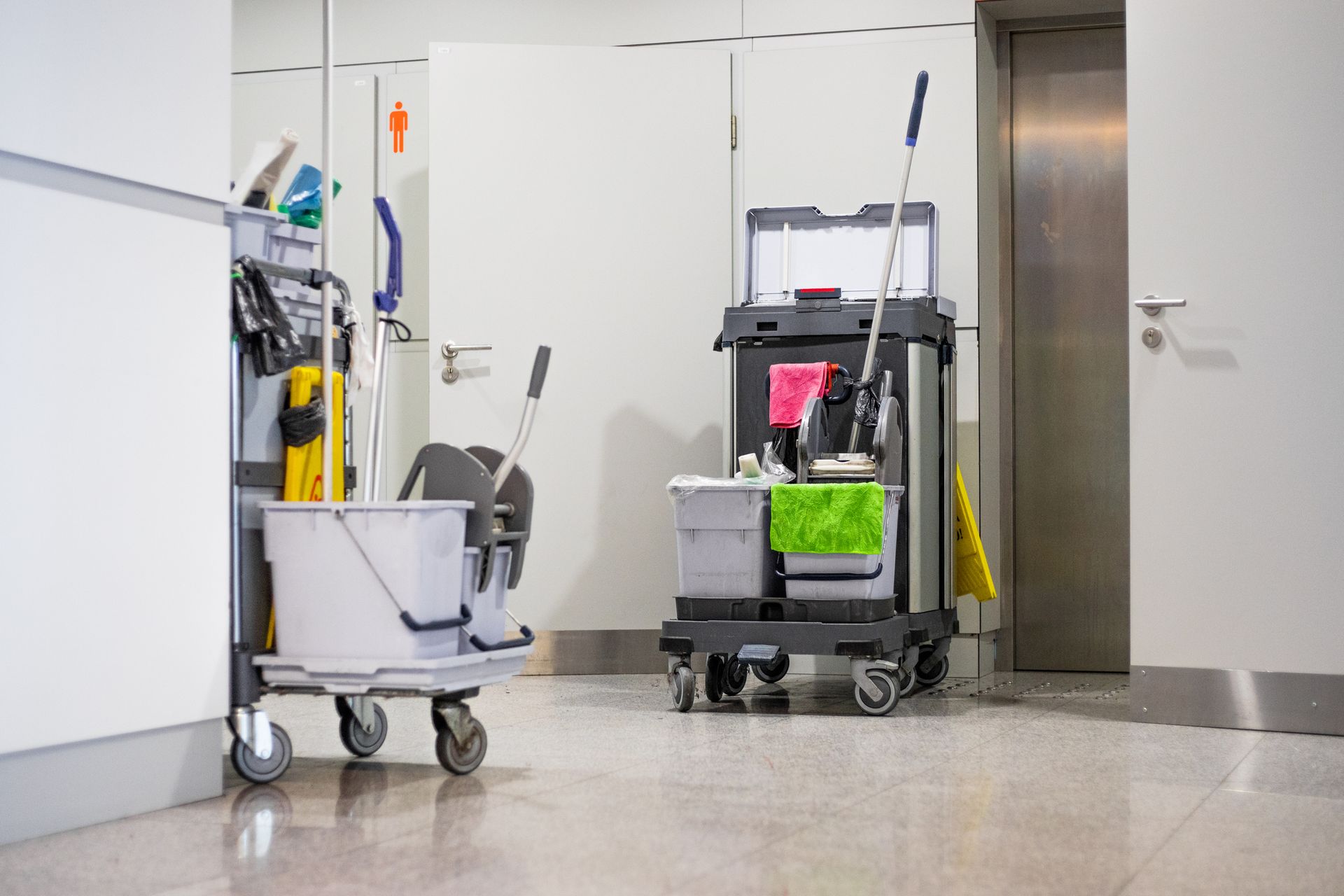 Cleaning cart with tools, cleaning buckets and cleaning equipment standing near restroom door.