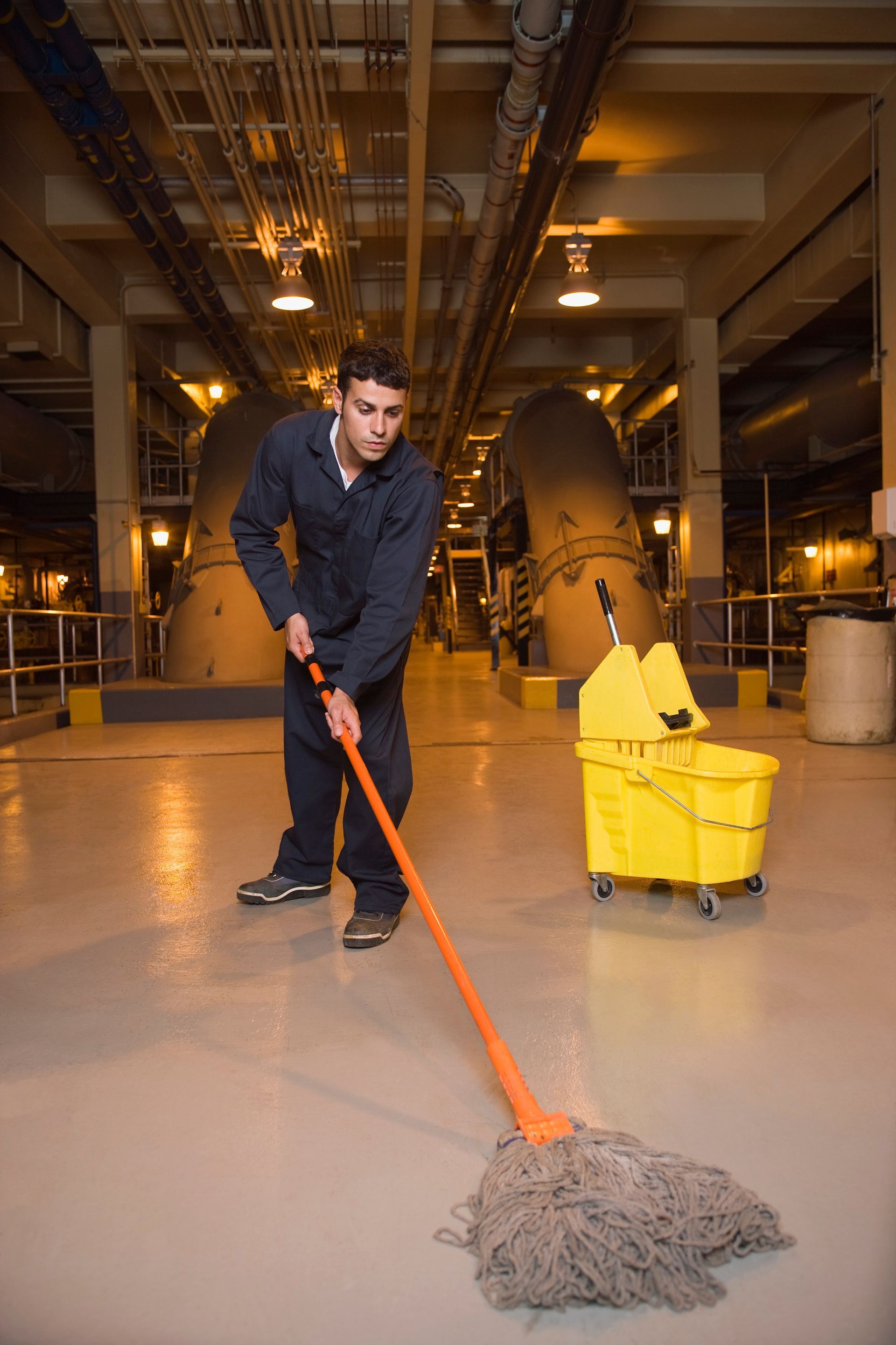 Male janitor in blue uniform mops the floor of a waste treatment plant.