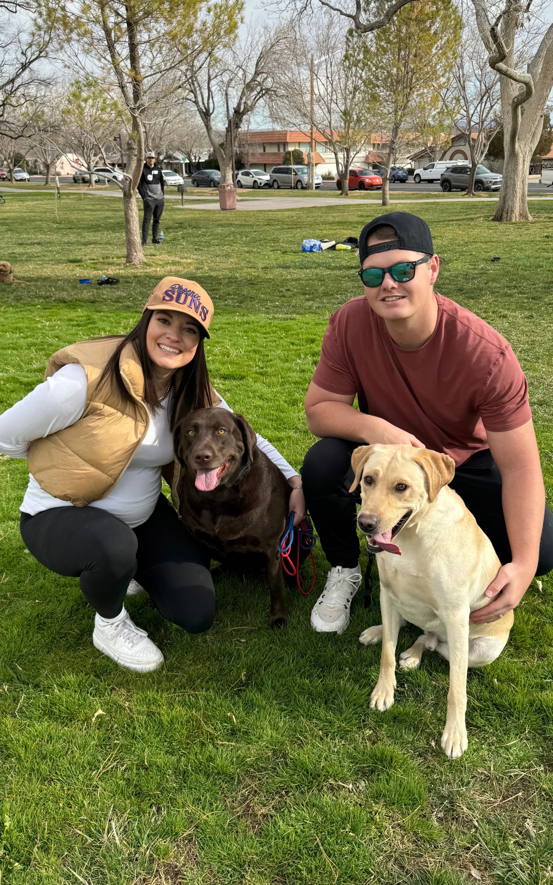 Dog owners next too their dogs in a down stay. The dogs are very happy and calm. They family is currently at CKC group class.