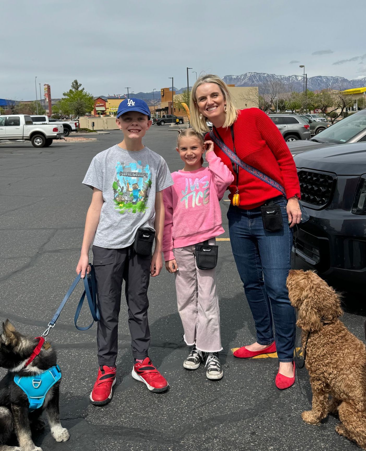 A mother with her two children smiling while their puppies are in a down stay. The dogs are calm and looking at the owner.