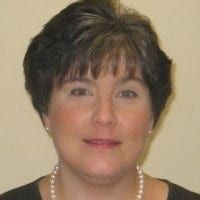 Woman with short, dark hair, wearing a pearl necklace, smiling.