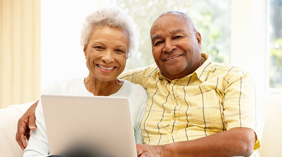 Smiling couple looking at laptop, indoors. Man's arm around woman.