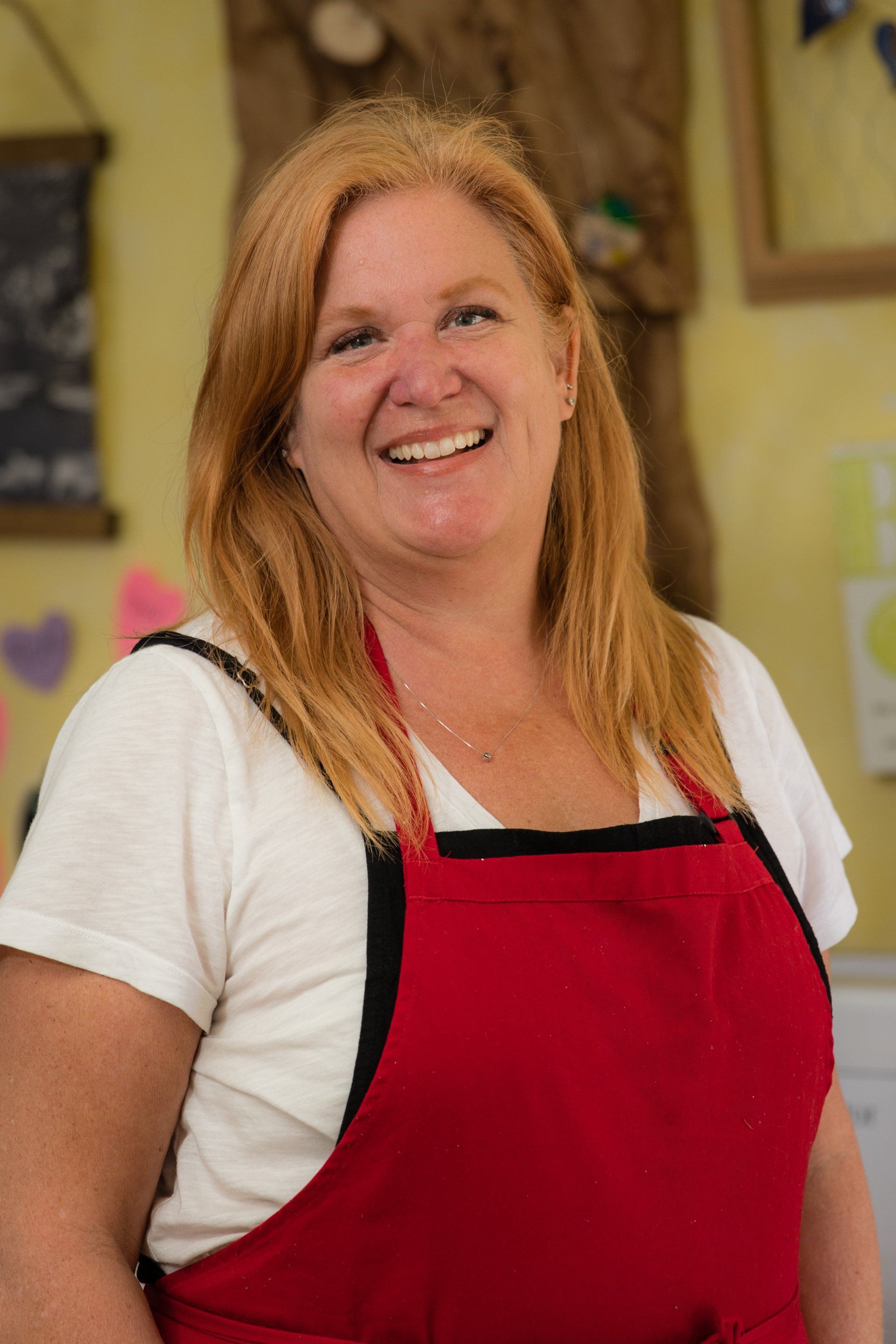 A woman wearing a red apron and a white shirt is smiling.