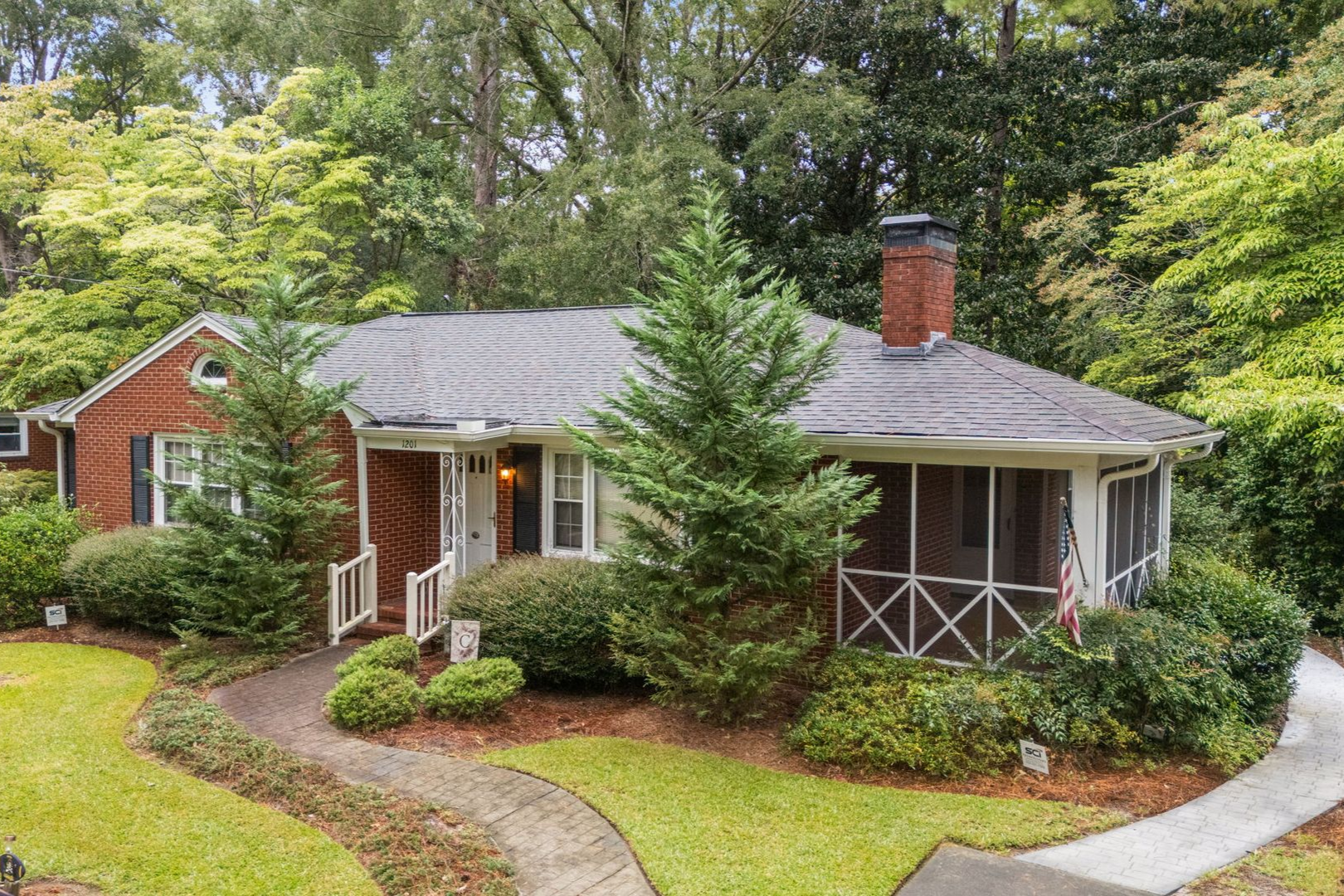 A small white house with blue shutters is surrounded by trees and grass.