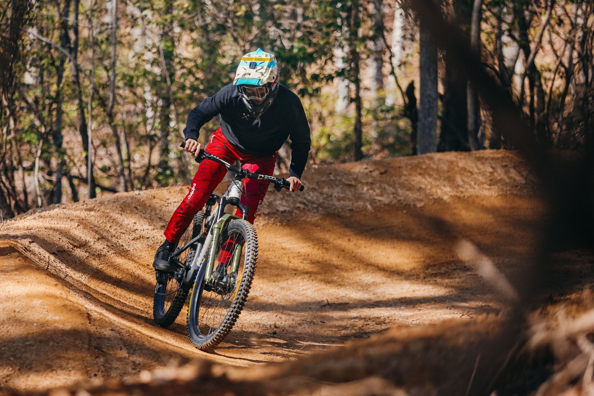 Mountain biker in silhouette jumps a dirt trail against a mountain backdrop.