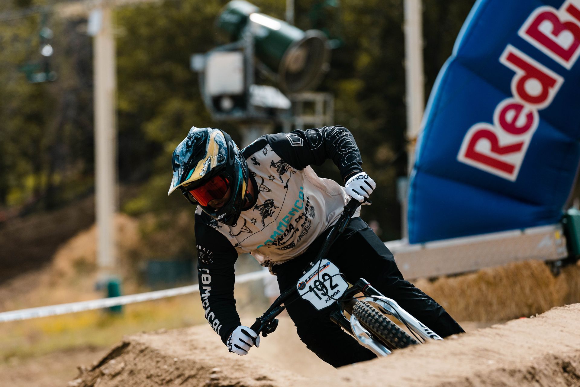 Mountain biker wearing helmet and gear navigating a turn at a race; Red Bull banner in background.