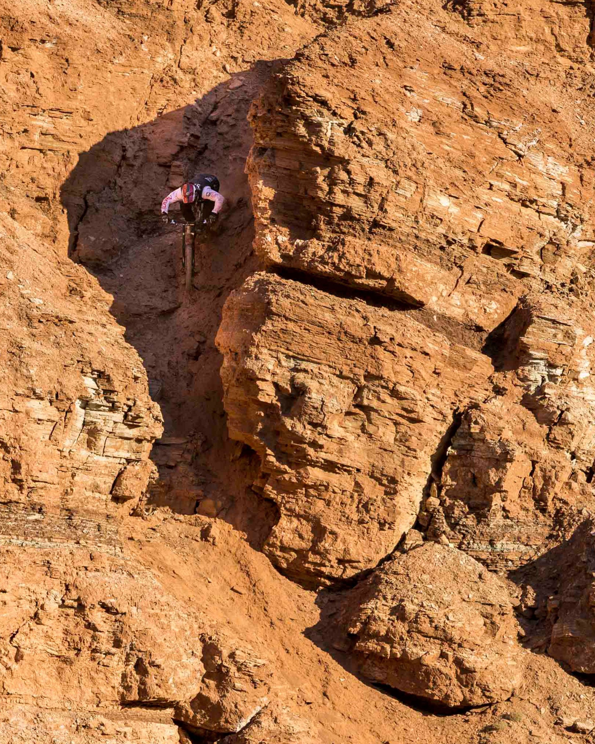 Rock climber scaling a reddish-brown cliff face.