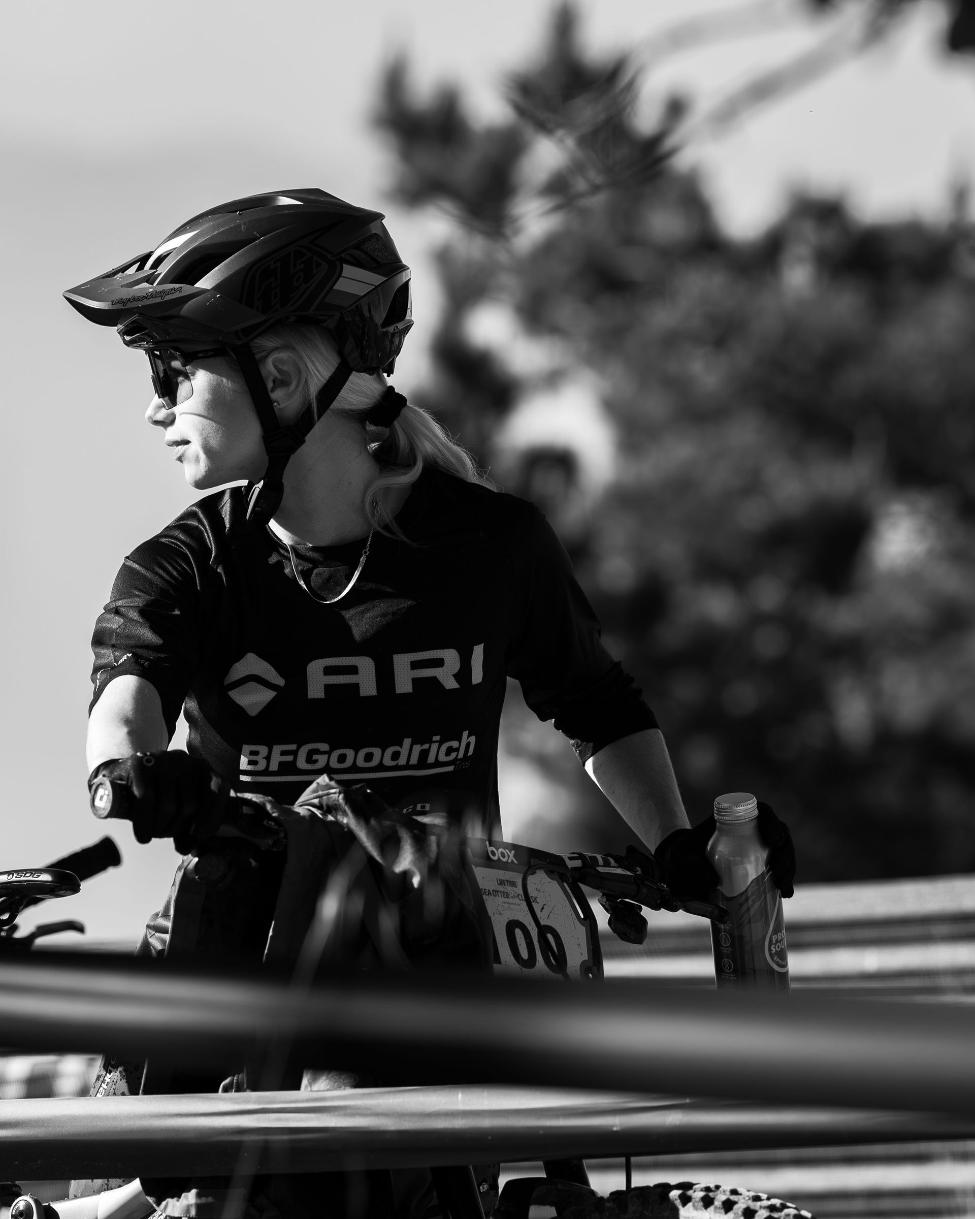 Mountain biker in helmet, looking back, holding bike, black and white.