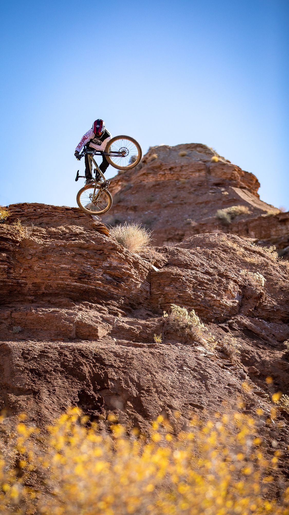 Mountain biker airborne on a rocky outcrop under a clear blue sky.