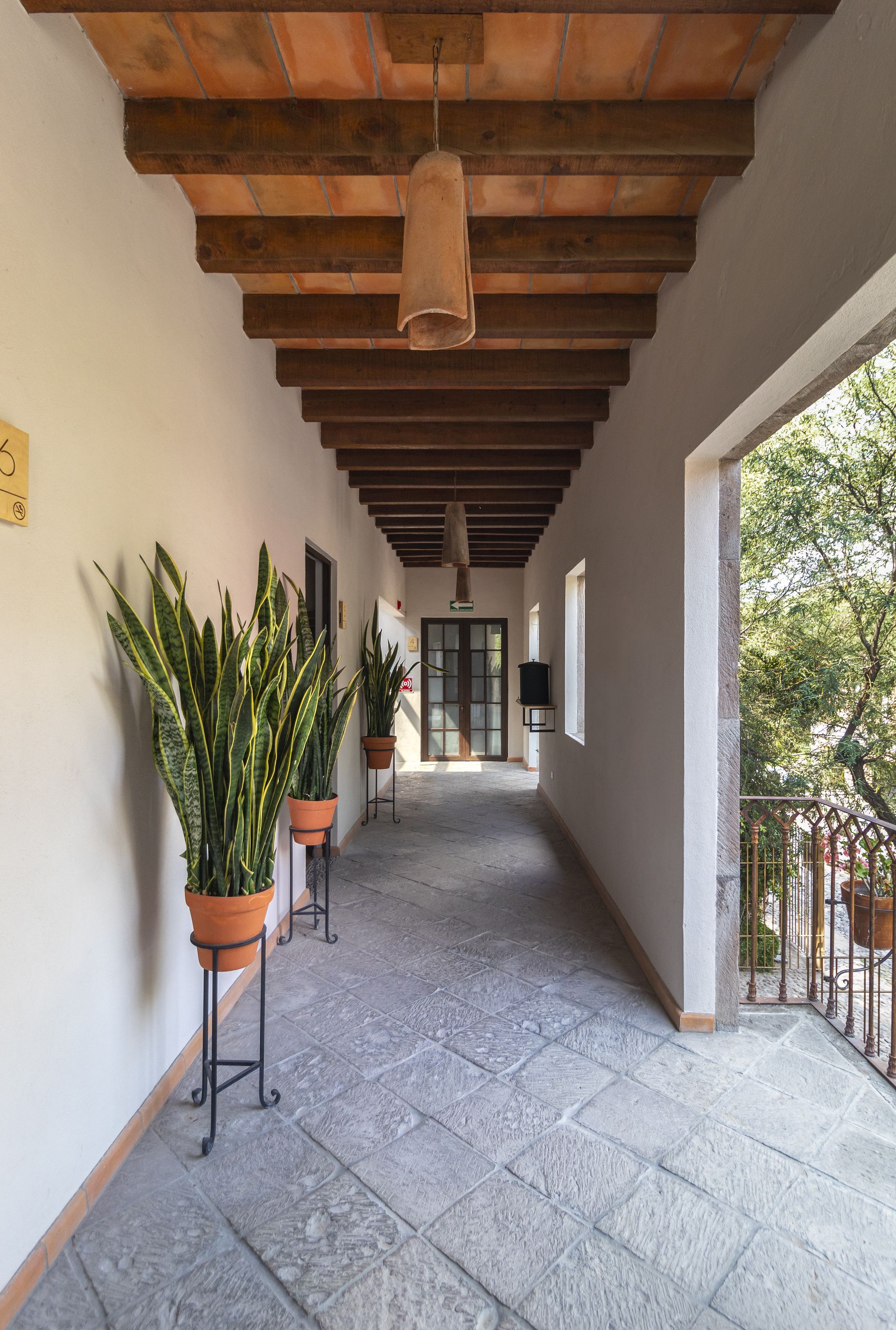 A long hallway with potted plants on stands and a wooden ceiling.
