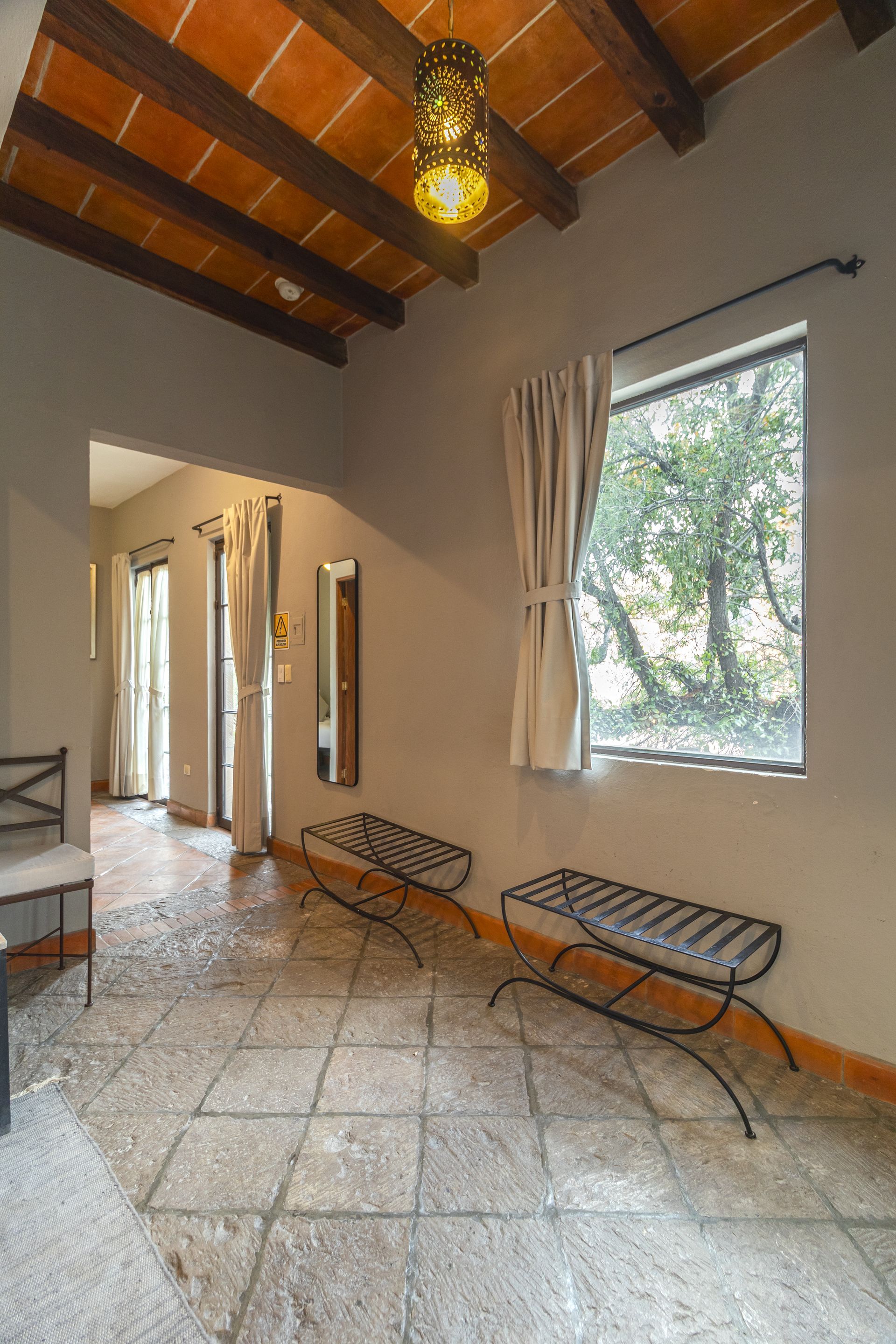 A living room with a tiled floor , chairs , benches and a window.