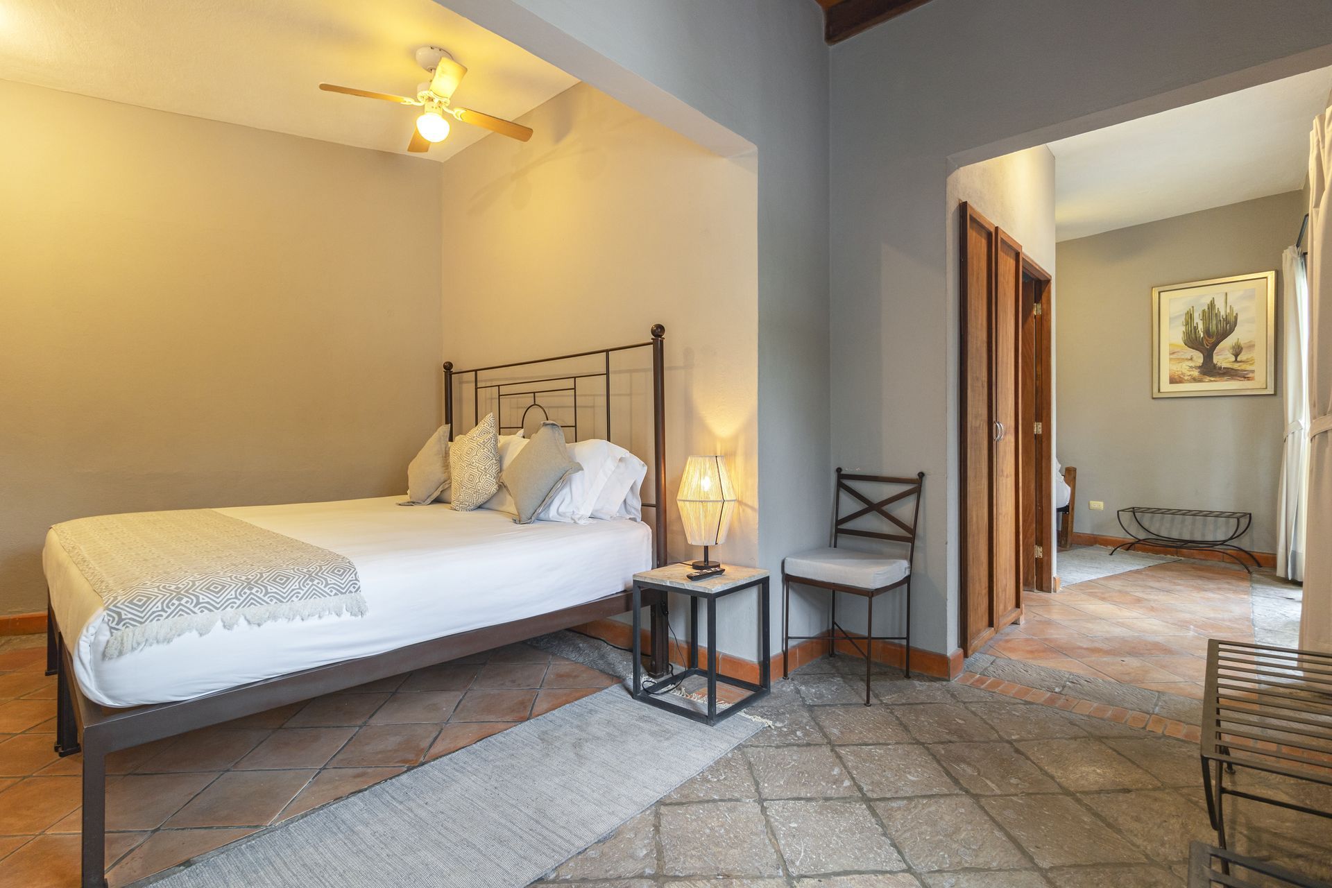 A bedroom with a bed , chair , table and ceiling fan.